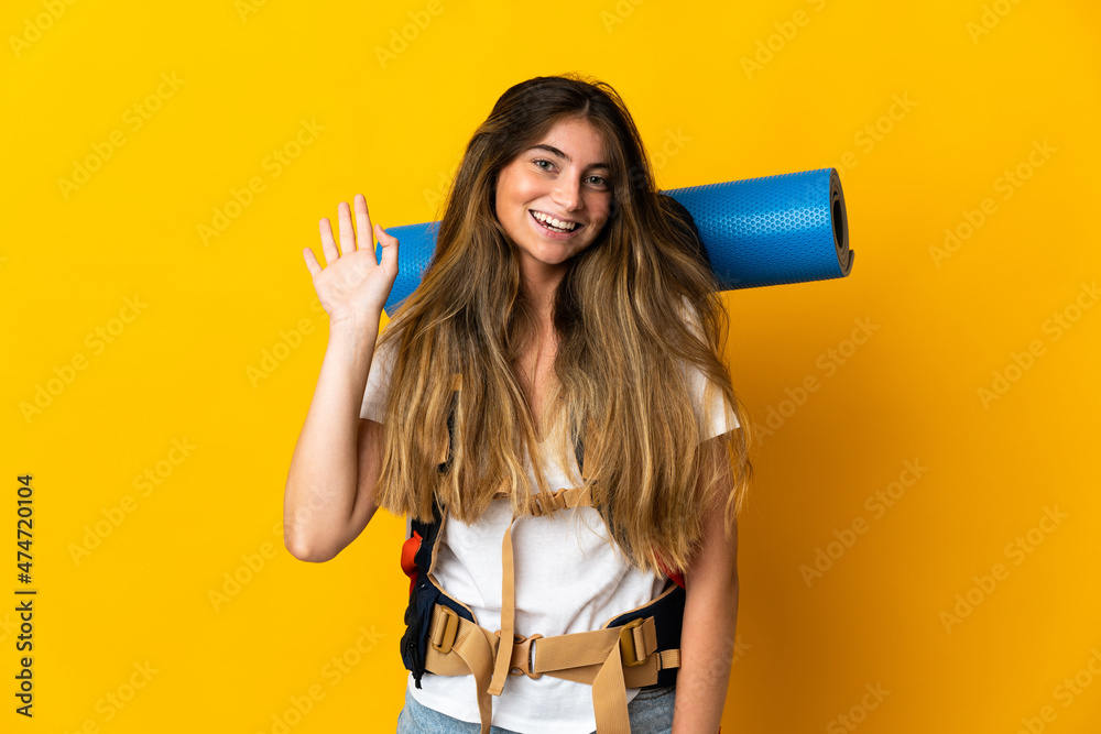 Young mountaineer woman with a big backpack isolated on yellow background saluting with hand with happy expression Young mountaineer woman with a big backpack isolated on yellow background saluting with hand with happy expression