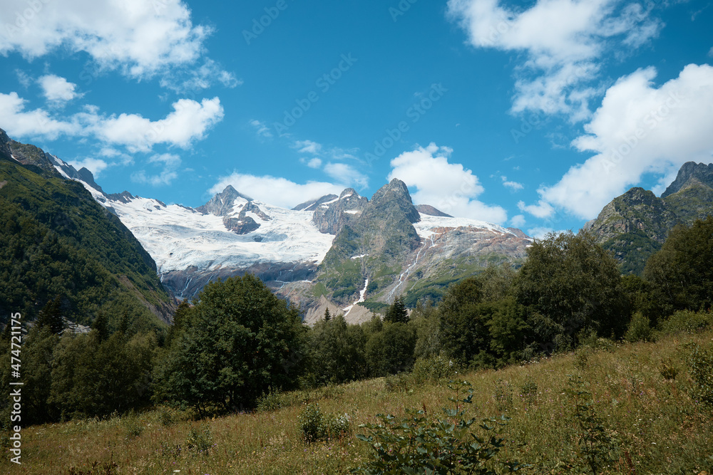 Landscape, mountain panorama, alpine meadows and mountain peaks in ice, a small house on the mountainside