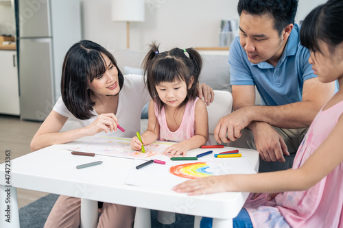 Asian young kid daughter coloring and painting on paper with parents. 