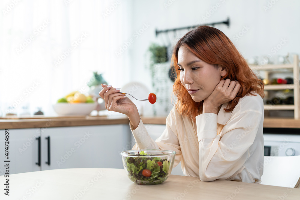 Asian young happy attractive woman eat green salad in kitchen at home.