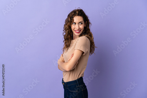Young caucasian woman isolated on purple background looking to the side and smiling © luismolinero