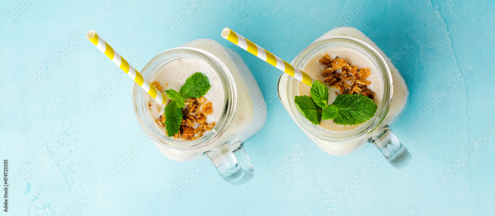 Banana smoothie with granola, dried fruits and mint on gray concrete background. Top view