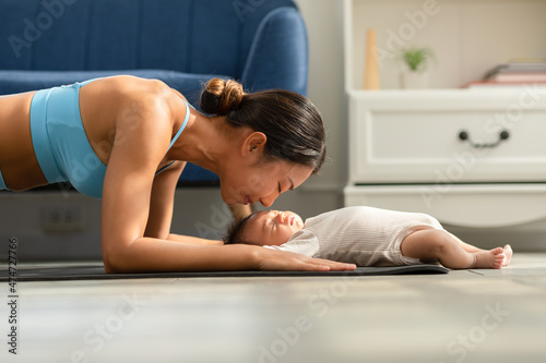 Side view of Wellness Asian woman mom doing plank exercise and kissing her baby at cozy home.Happy healthy mother yoga plank with newborn baby boy sleep and lying on yoga mat.Yoga Mom and Baby Concept