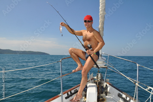 Happy tourist in sunglasses posing on yacht with caught fish in gulf of Thailand