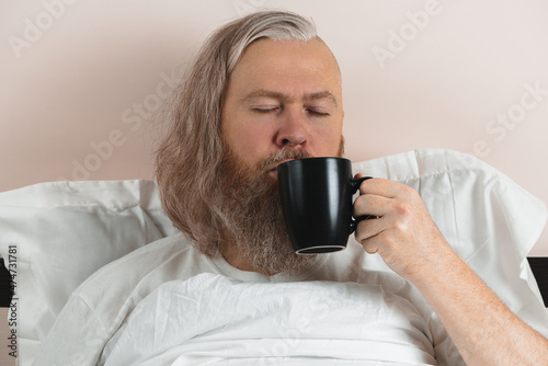 Obraz na płótnie Bearded man enjoying his morning coffee in bed to cheer up before starting new day. Closeup. w salonie