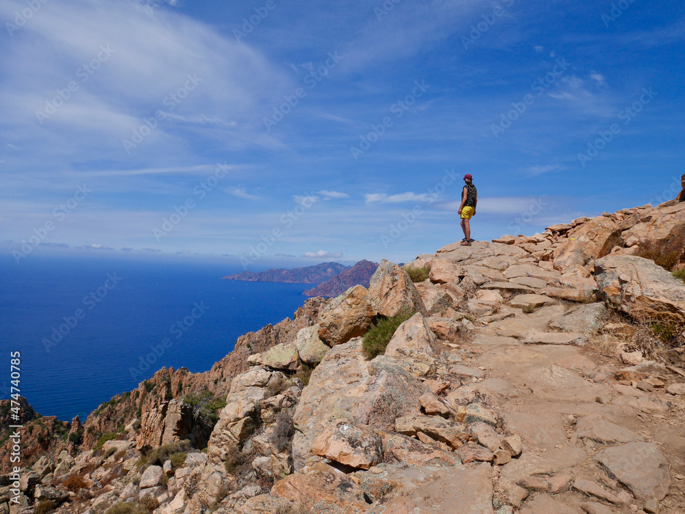 Woman looking at the red cliffs of the Calanche, UNESCO world heritage, and the Golf of Porto. Corsica, France.