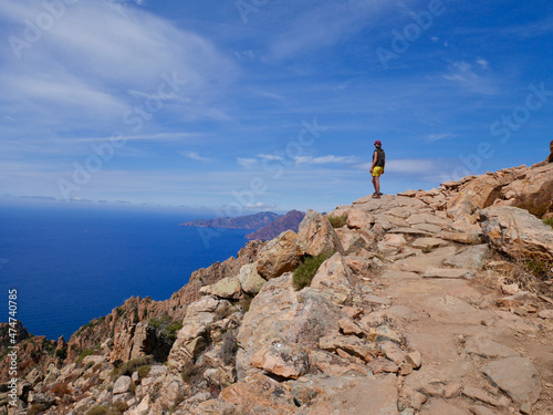 Woman looking at the red cliffs of the Calanche, UNESCO world heritage, and the Golf of Porto. Corsica, France.