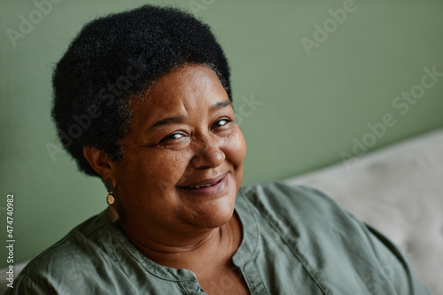 Portrait of black senior woman smiling at camera against green background at home, copy space