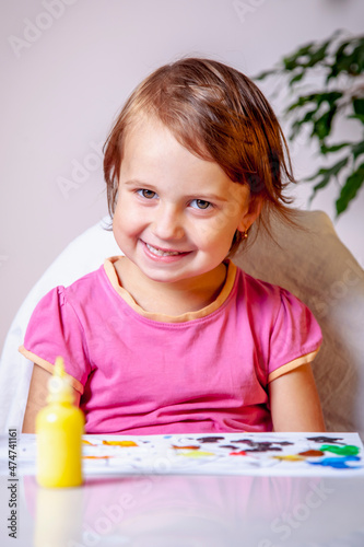 Portrait of cute little girl drawing with colorful paint. Beautiful adorable child painting at table. Vertical image.