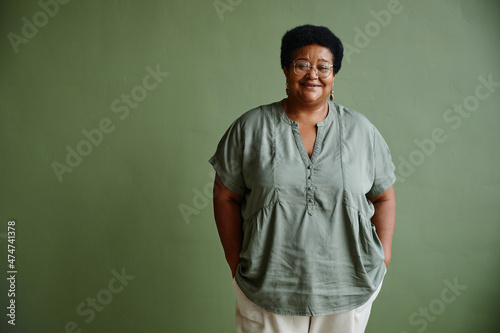 Waist up portrait of black senior woman smiling at camera while standing against green background, copy space © Seventyfour