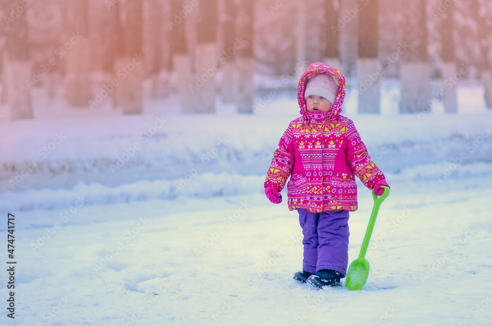Caucasian little girl of 2 years in winter park with toy shovel with copy space