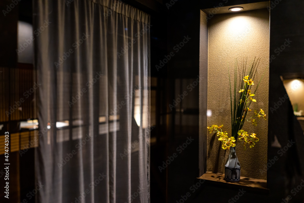 Traditional Japanese house or ryokan home hotel with yellow flower ikebana in vase decoration decor illuminated by lamp in dark room with curtains at night