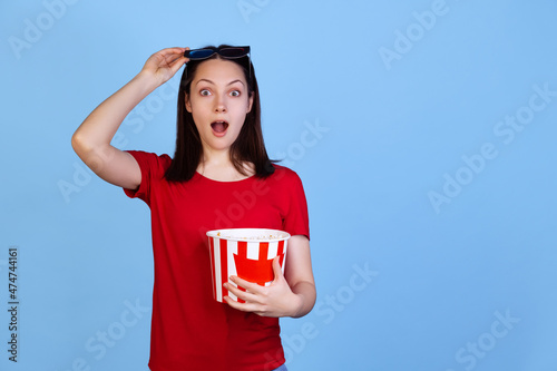 Half-length portrait of excited young girl in red t-shirt watching 3D movie isolated on blue studio background. Concept of emotions