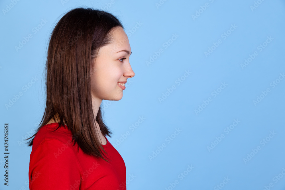 Profile view of pretty young woman in red t-shirt isolated on blue studio background. Concept of emotions