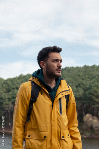 A boy with yellow raincoat standing in front of the lake. He has camp chair on his hand. He will have a rest by the lake. Nature park on a gold autumn day. He admires autumn nature landscape.