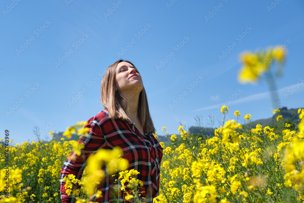Happy woman enjoying nature, sunlight touching her face and breathing fresh air, in the middle of a beautiful field full of yellow flowers. rapeseed in spring. (Brassica napus) Happy woman enjoying nature, sunlight touching her face and breathing fresh air, in the middle of a beautiful field full of yellow flowers. rapeseed in spring. (Brassica napus)