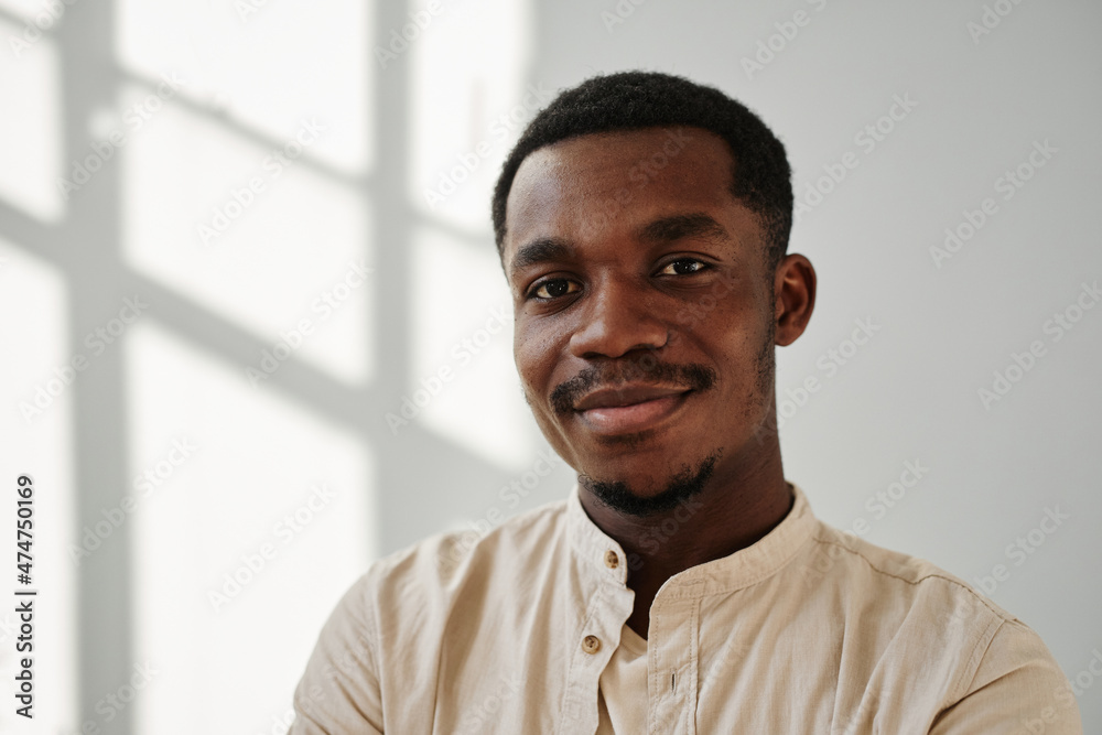 Portrait of African young man in casual shirt smiling at camera against the white wall Portrait of African young man in casual shirt smiling at camera against the white wall