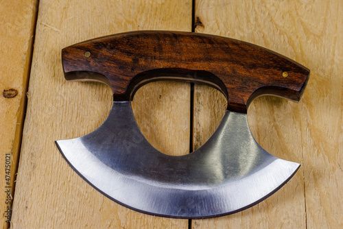 Close up of a Ulu knife with a wood handle on pine boards. Traditionally used by Inuit (Eskimo) women and is an all-purpose knife. 
