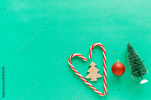 Christmas candy canes in heart shape with decorations on green background. Minimalistic holiday flatlay with copy space for text.