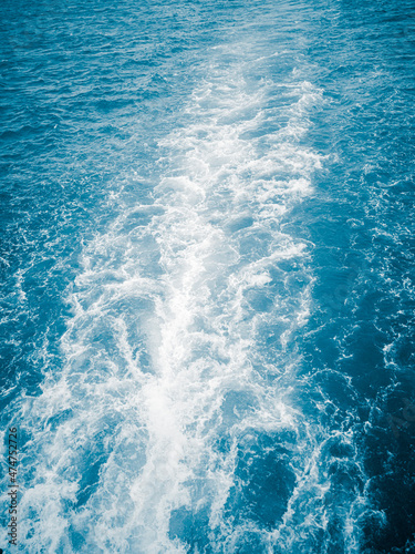 A white wave and foam on blue water, a divergent trail from the boat