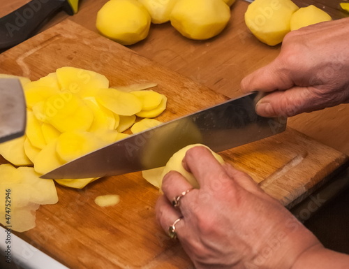 Women's hands cut potatoes with a knife on a wooden board close-up