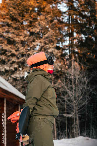 Winter sports. Portrait of a snowboarding girl against the background of a wooden house and a winter forest.