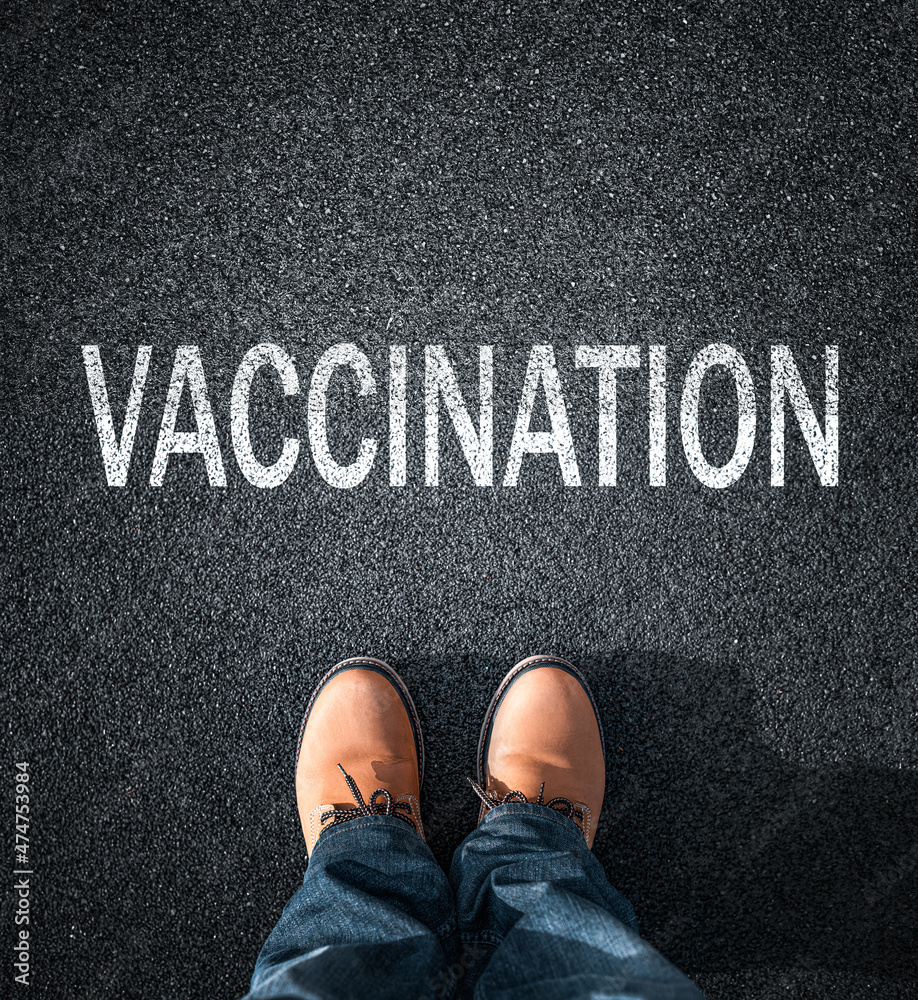 Inscription Vaccination on the asphalt. Feet in boots against the background of the inscription about vaccination. The choice of a person to be vaccinated.