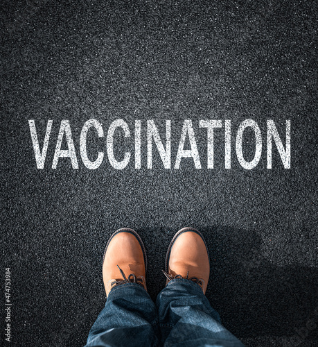 Inscription Vaccination on the asphalt. Feet in boots against the background of the inscription about vaccination. The choice of a person to be vaccinated.