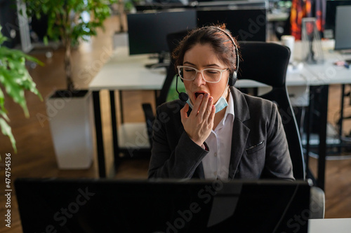 Business woman in a medical mask yawns at her desk in the office.