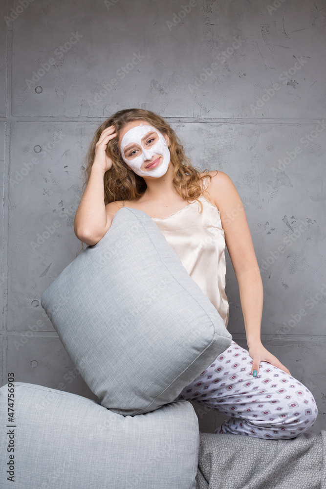 Fototapeta premium The girl sits on the sofa wearing a cosmetic mask.