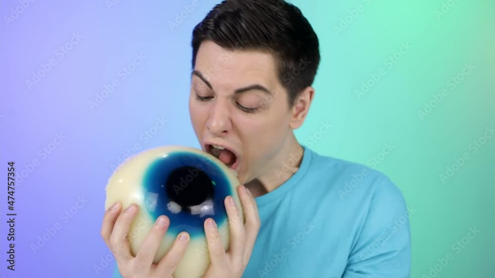 Hungry young man eating a big gelatinous eye. An attractive guy holds a delicious gelatinous candy in his hands. Hungry young man eating a big gelatinous eye. An attractive guy holds a delicious gelatinous candy in his hands.