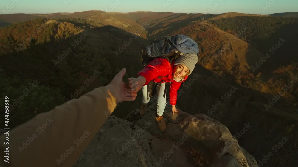 Close up of male's hand stretching out and helping female hiker reach cliff top by pulling her up from edge. POV of man giving hand to woman climbing on cliff and helping her reach top. autumn hike.