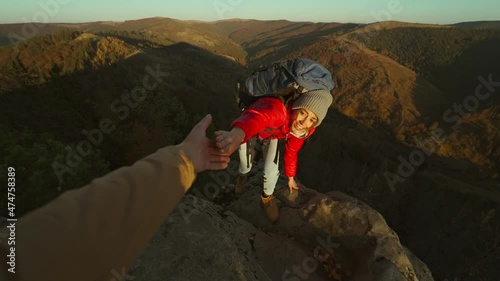 Close up of male's hand stretching out and helping female hiker reach cliff top by pulling her up from edge. POV of man giving hand to woman climbing on cliff and helping her reach top. autumn hike.