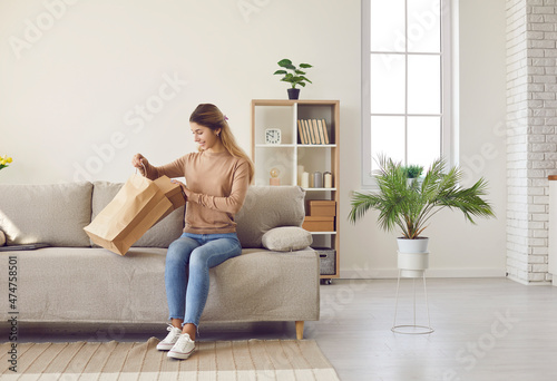 Smiling young woman sit on couch do unpacking at home shopping online. Happy girl client or customer on sofa unbox unpack parcel buy on internet. Good delivery service concept. International shipping.