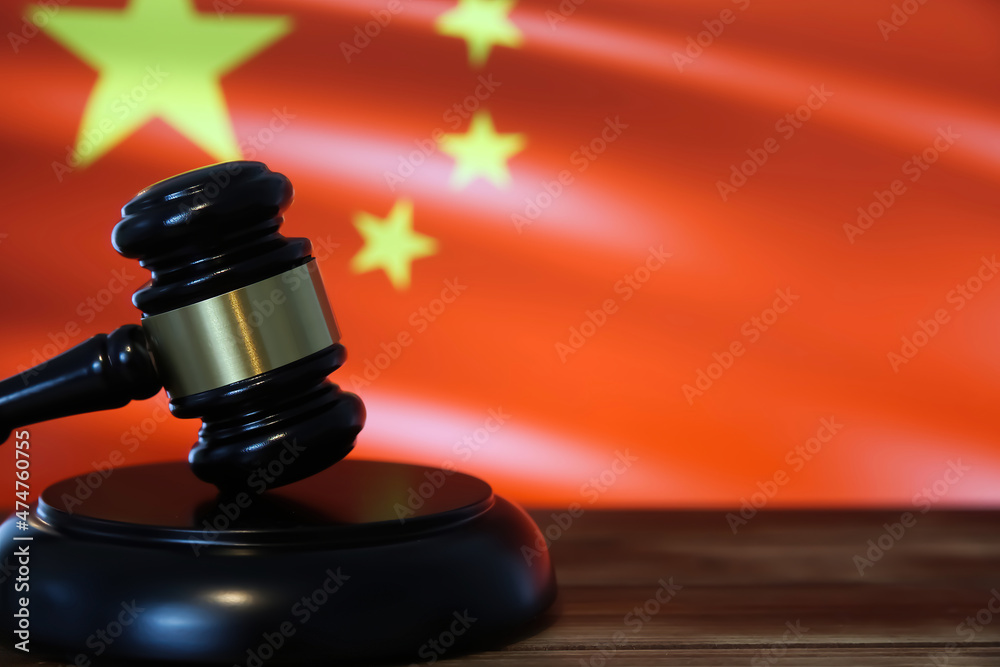 Closeup of isolated judge wood gavel with blurred chinese flag background (focus on hammer head)