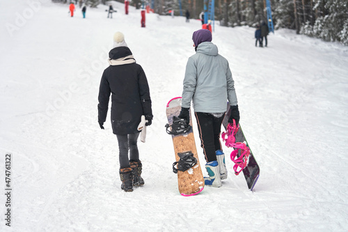 Ski resort. A guy and a girl climb a snowy mountainside. The guy carries two boards. A t-bar lift passes to their right. Selective focus.