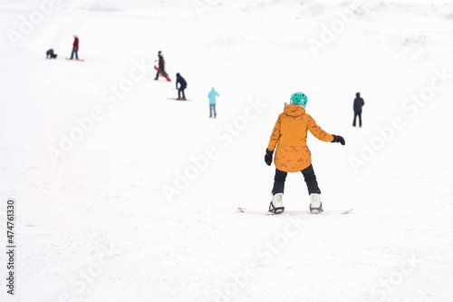 A girl is snowboarding down a snow-covered mountainside. Below there are already descended snowboarders and skiers. Selective focus.