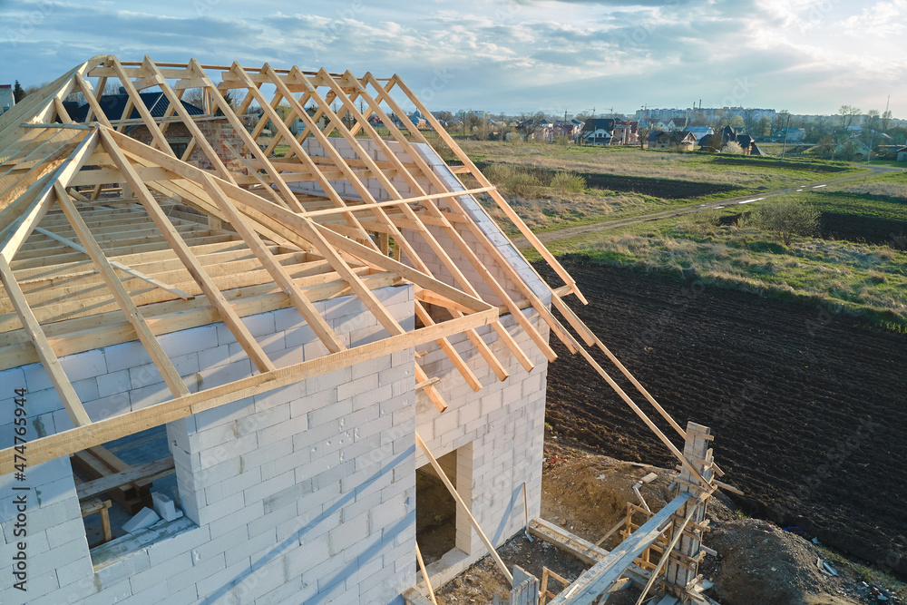Obraz premium Aerial view of unfinished frame of private house with aerated lightweight concrete walls and wooden roof frame under construction