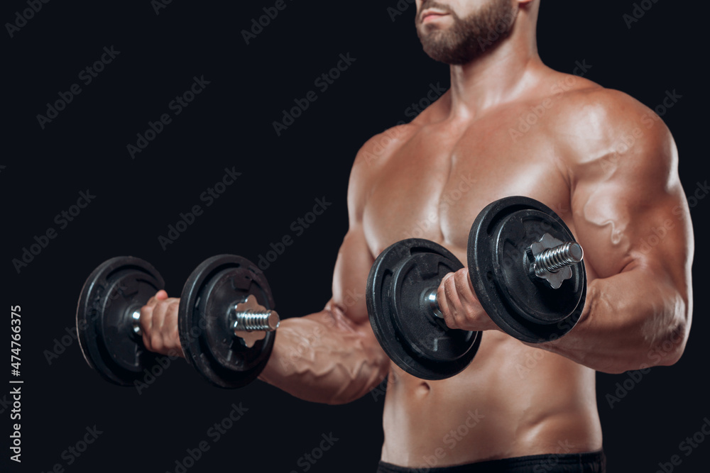 Close up of muscular body and strong hands lifting heavy dumbbells isolated over black background