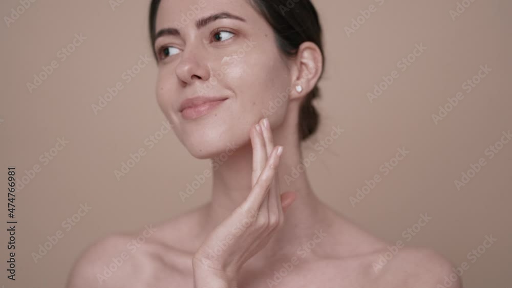 Portrait of pretty woman applying skin care cream on her face to make face soft and fresh over beige color background Portrait of pretty woman applying skin care cream on her face to make face soft and fresh over beige color background