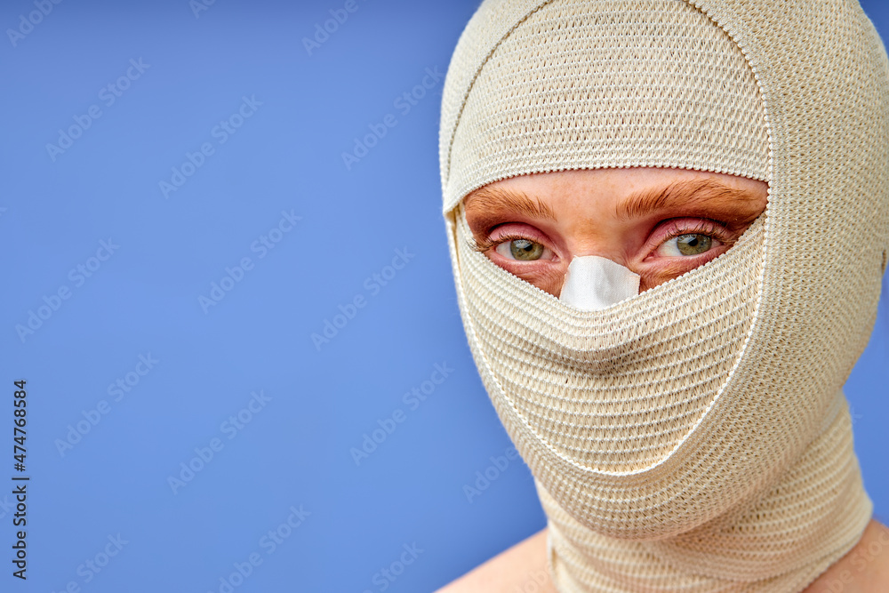 Beautiful caucasian woman after plastic surgery with bandaged face, isolated on blue background. unrecognizable lady after rhinoplasty. beauty treatment plastic surgery concept