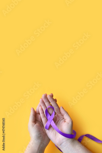 International Epilepsy Day. Adult hands holding purple ribbon on yellow background. Alzheimer's disease, Pancreatic cancer, Hodgkin's Lymphoma awareness
