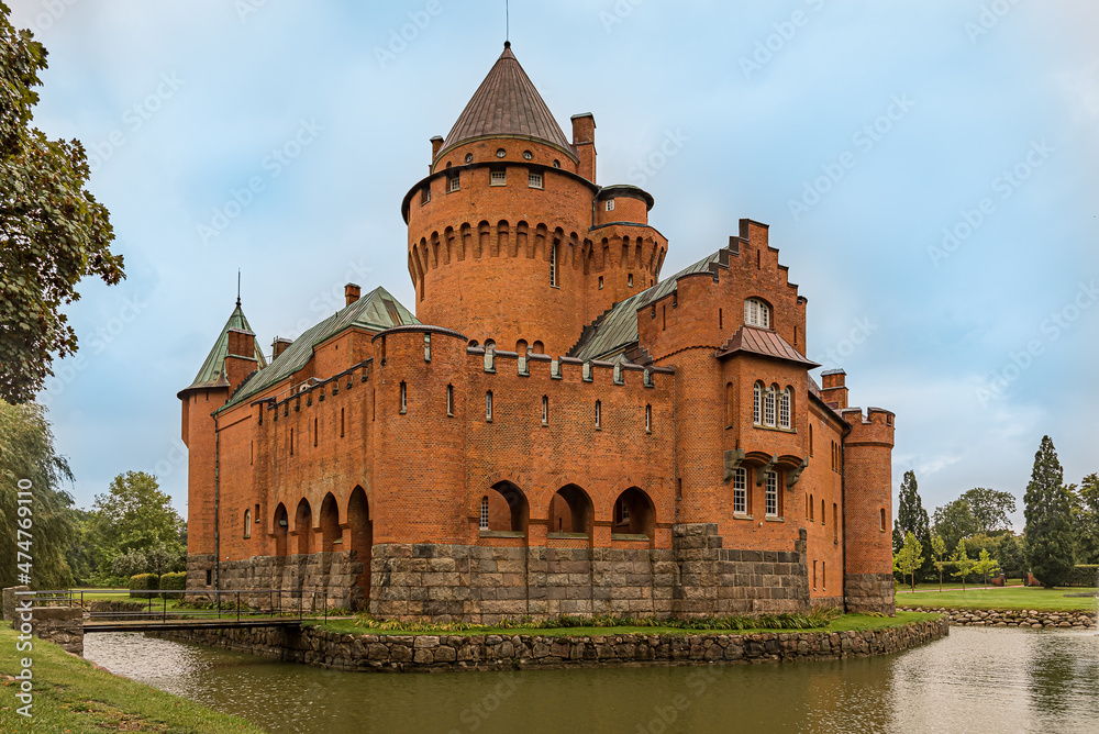a romantic red castle with a tall tower surrounded by a moat