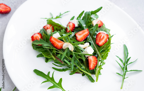 Romantic salad of strawberry with mix of herbs, arugula, spinach leaves, feta cheese and cashew nuts in heart shape on white plate. Romantic meal for St Valentine Day celebration.