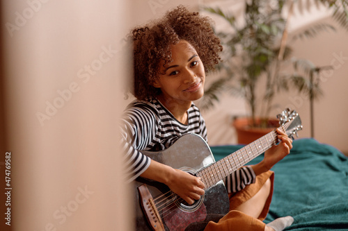 Multiracial young woman looking at camera and smiling while playing melody on acoustic musical instrument photo