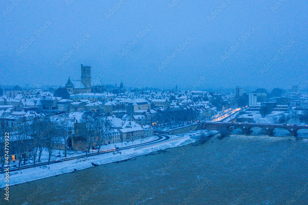 Fototapeta premium The city center of Nevers and its Loire bridge under the snow in Europe, France, Burgundy, Nievre, in Winter, during a cloudy evening.