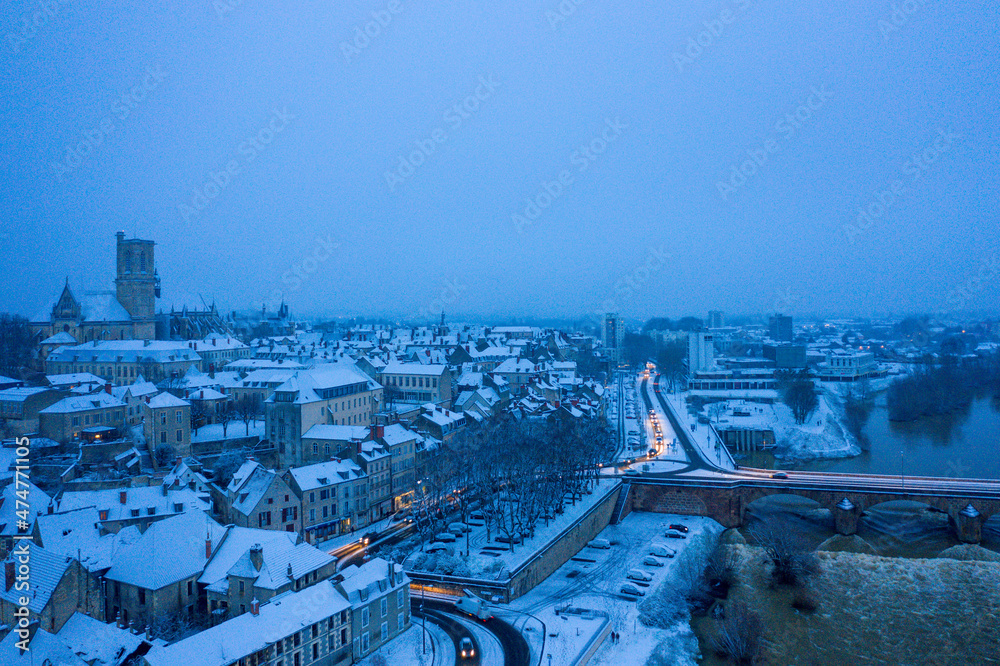 The city center of Nevers on the banks of the Loire under the snow in Europe, France, Burgundy, Nievre, in Winter, during a cloudy evening.