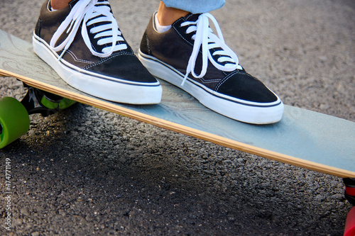 Teenager rides a skateboard on the street in sneakers and jeans, while sun is shining. Street sports and leisure for young people