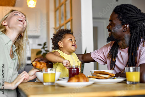 beautiful caucasian family of man and woman sitting together talking with daughter while eating healthy breakfast at home, in cozy bright room. excited family have fun while having meal