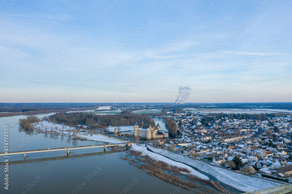 The town center of Sully sur Loire and its medieval castle under the snow in Europe, in France, in the Center region, in the Loiret, towards Orleans, in Winter, on a sunny day.